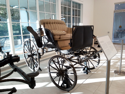 [This phaeton is a two-seater carriage with black wheels and the front ones are smaller than the rear ones. The inners are tan tuffed cushions. The front and sides appear to be black metal.]